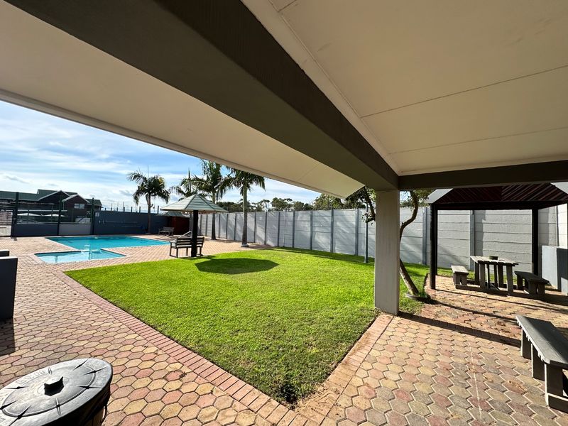 A spacious covered patio overlooking a well-maintained garden, swimming pool, and outdoor gazebo area, perfect for outdoor entertaining.