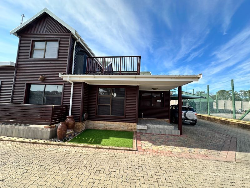 Front exterior view of a timber-clad house featuring a paved driveway, covered patio area, and an upper-level balcony.