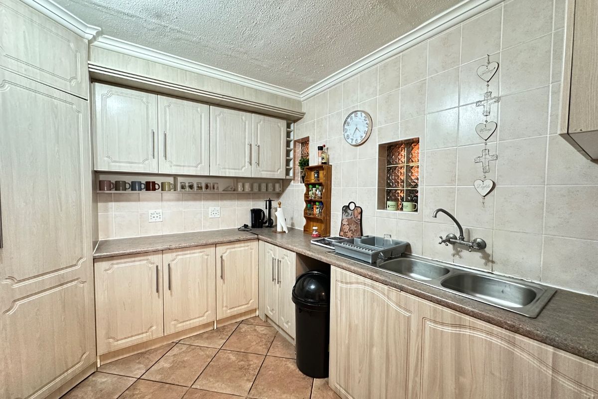 A functional kitchen featuring light wood-look cabinetry, laminate countertops, a double stainless steel sink, and neutral ceramic wall and floor tiling.