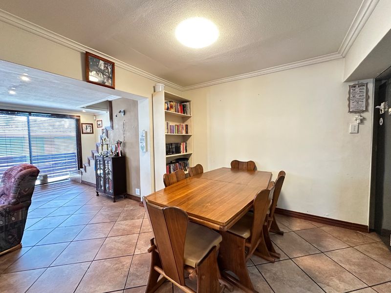 A dining area featuring tiled flooring, coved cornicing, and built-in shelving, seamlessly connected to an adjacent living space.