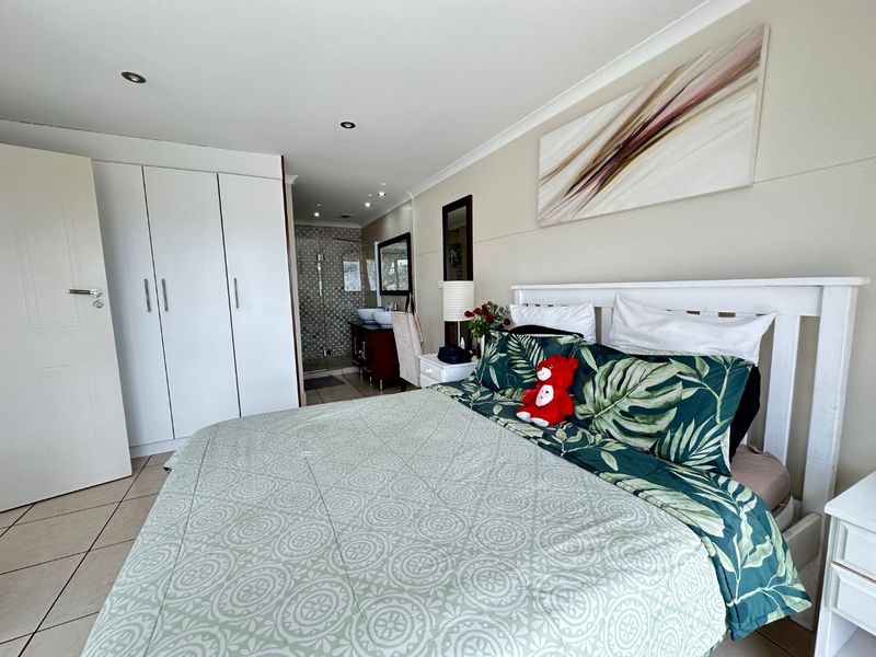 A well-maintained bedroom featuring built-in cupboards, tiled flooring, recessed lighting, and an open-plan en-suite bathroom with a double vanity and glass shower.