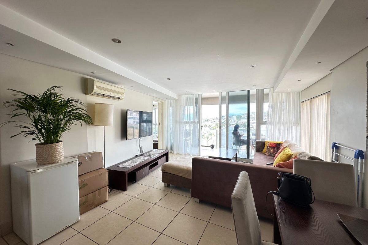 Spacious living area featuring tiled flooring, recessed ceiling lights, and large sliding glass doors leading to a balcony with natural light.