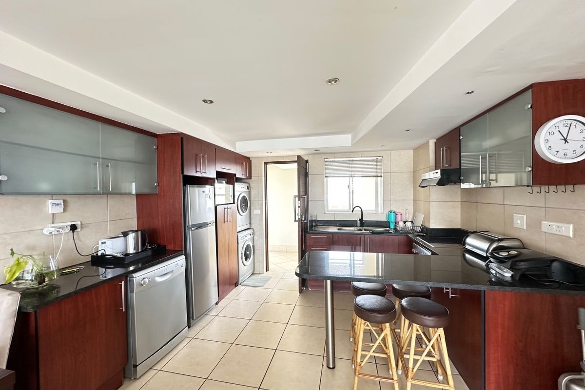 A functional kitchen featuring dark wood cabinetry, granite countertops, a breakfast bar, and integrated laundry appliances, offering a practical layout for daily use.