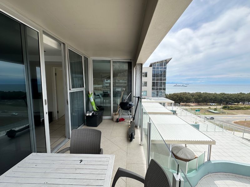 Spacious covered balcony featuring tiled flooring and a glass balustrade, offering expansive coastal and ocean views.