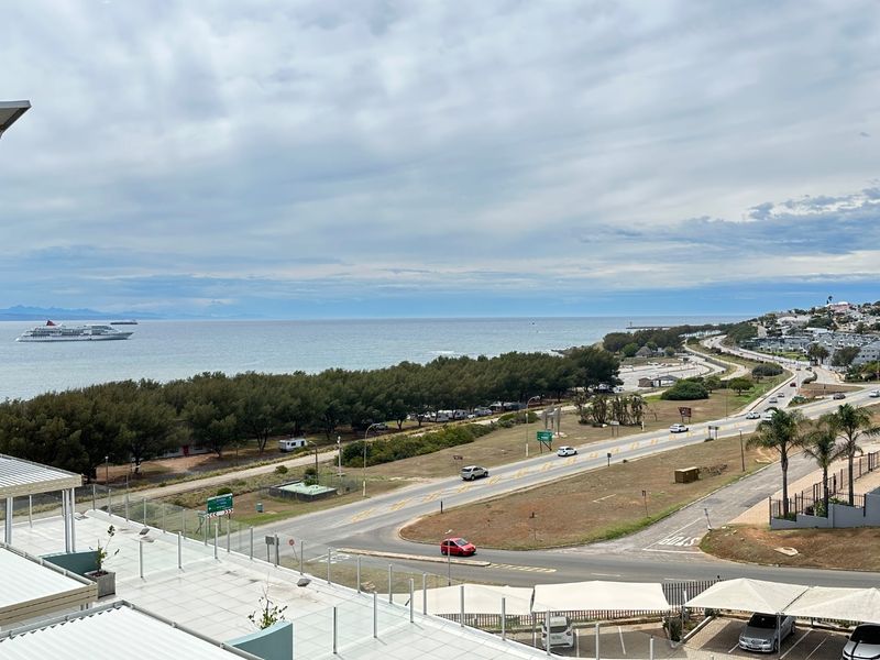 Elevated coastal view overlooking the ocean, coastal road, and surrounding landscape from a modern apartment balcony.