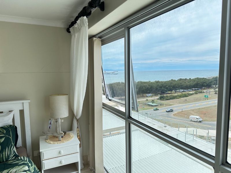 Bedroom featuring a large window with expansive coastal and road views, providing natural light and a scenic outlook.