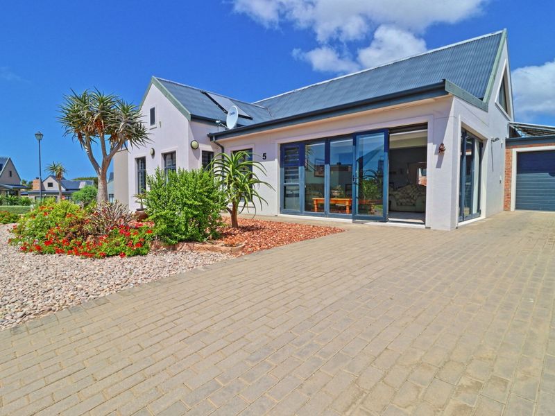 Front elevation of a modern house featuring a paved driveway, metal roof, and large bi-fold doors opening into the living area.