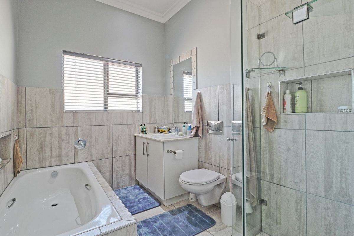 Modern bathroom featuring a built-in bathtub, glass-enclosed shower, wall-mounted toilet, and vanity cabinet with neutral tiled finishes.