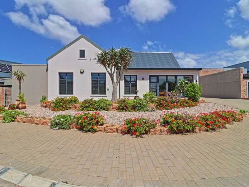 A well-maintained single-story house featuring a paved driveway, stone-edged garden beds, and modern aluminium window frames with a corrugated metal roof.