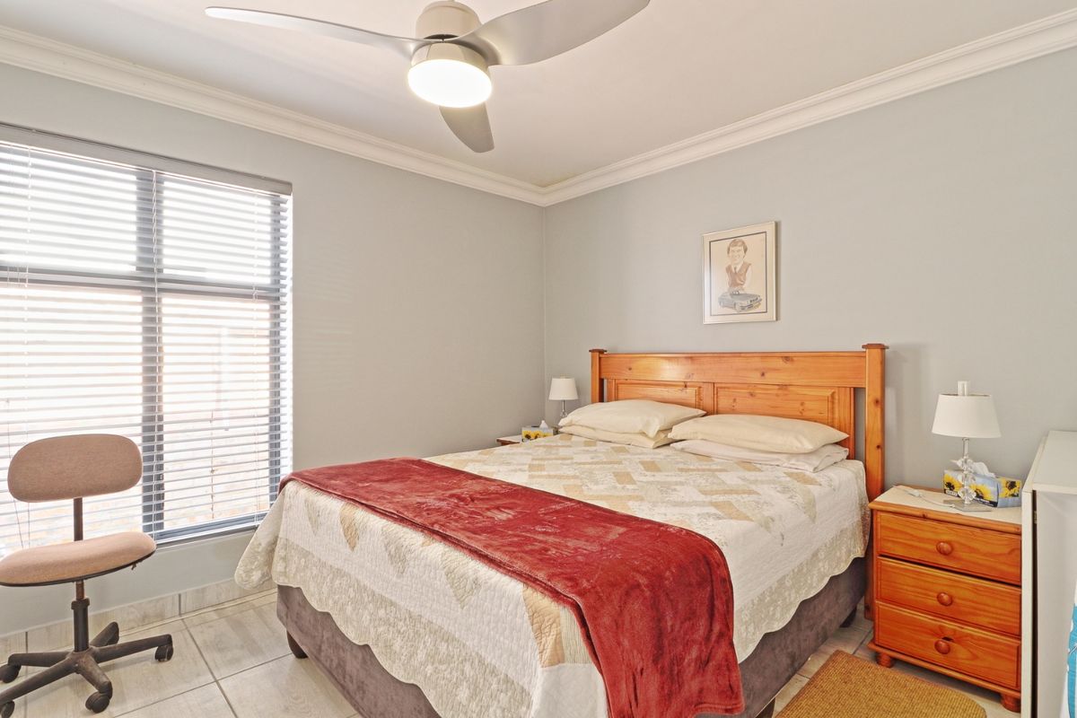 A well-maintained bedroom featuring tiled flooring, crown molding, and a modern ceiling fan, with natural light provided by a large window with venetian blinds.