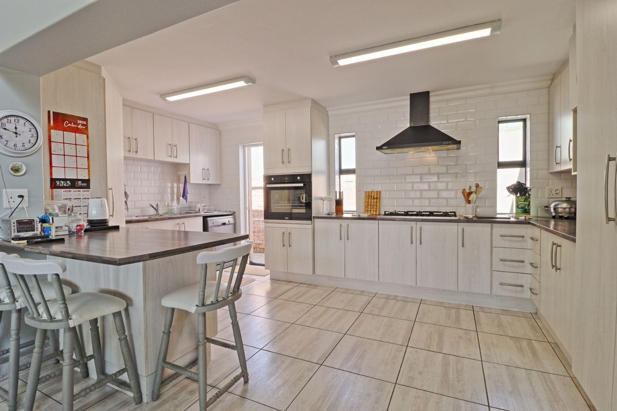 A well-maintained kitchen featuring light wood-grain cabinetry, subway tile backsplash, built-in oven, gas hob, and a functional breakfast bar with tiled flooring.