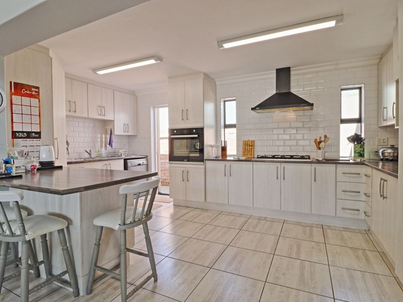 A well-maintained kitchen featuring light wood-grain cabinetry, subway tile backsplash, built-in oven, gas hob, and a functional breakfast bar with tiled flooring.