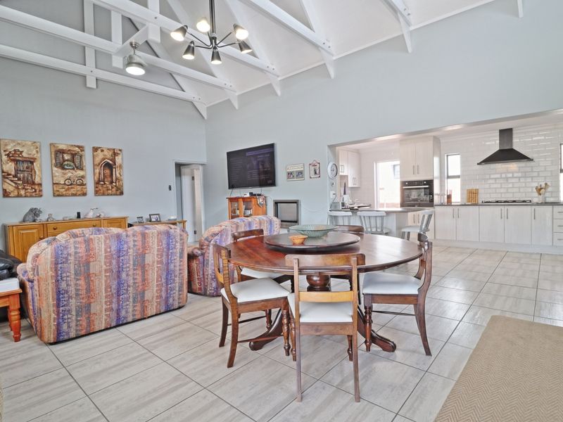Spacious open-plan living and dining area featuring vaulted ceilings with exposed rafters, flowing into a modern kitchen with subway tile backsplash and built-in appliances.