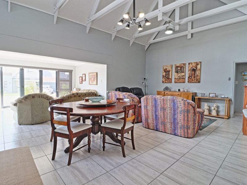Spacious open-plan living and dining area featuring high vaulted ceilings with exposed white trusses, tiled flooring, and large sliding doors leading to the exterior.