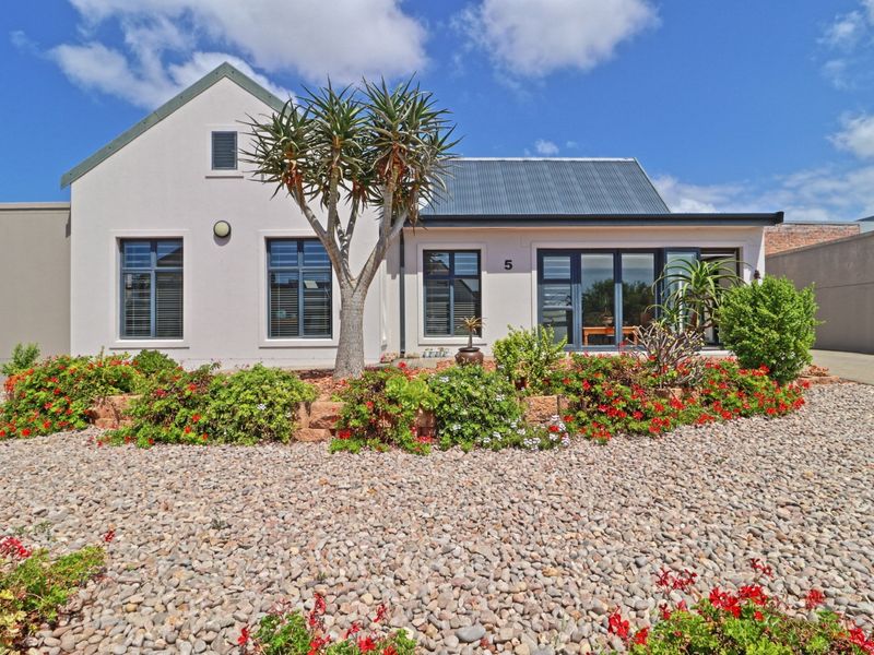 A well-maintained front facade featuring a modern corrugated roof, aluminium window frames, and neatly landscaped pebble garden beds.