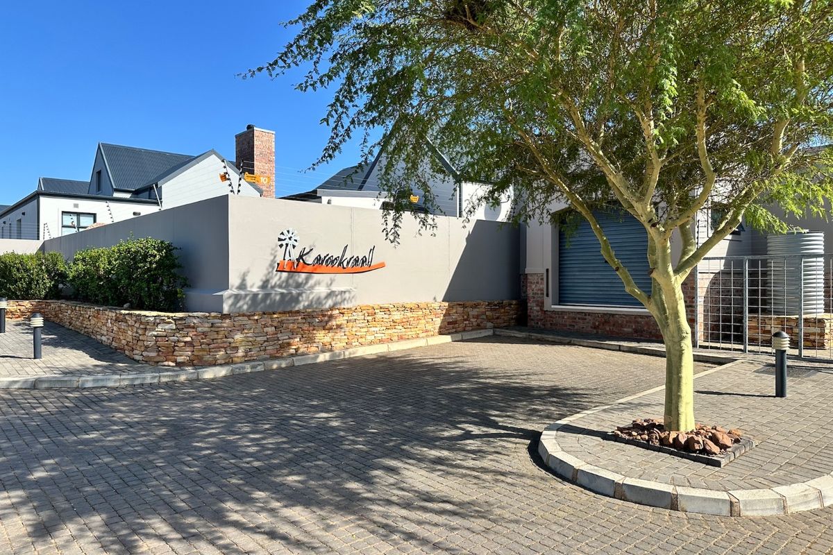 Front view of the property entrance featuring a paved driveway, stone-clad boundary wall, and secure roller shutter access.