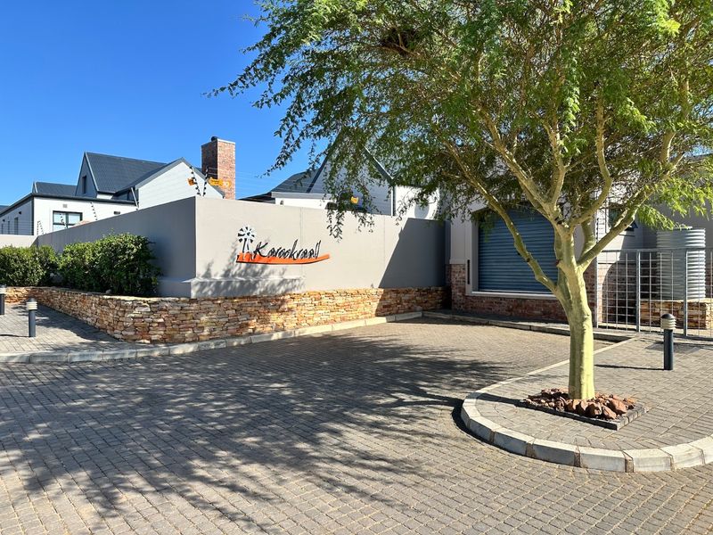 Front view of the property entrance featuring a paved driveway, stone-clad boundary wall, and secure roller shutter access.