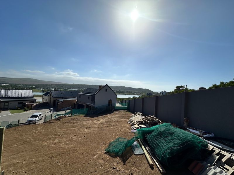 A vacant residential plot featuring a boundary wall and sloped terrain with views of the surrounding landscape and nearby residential properties.