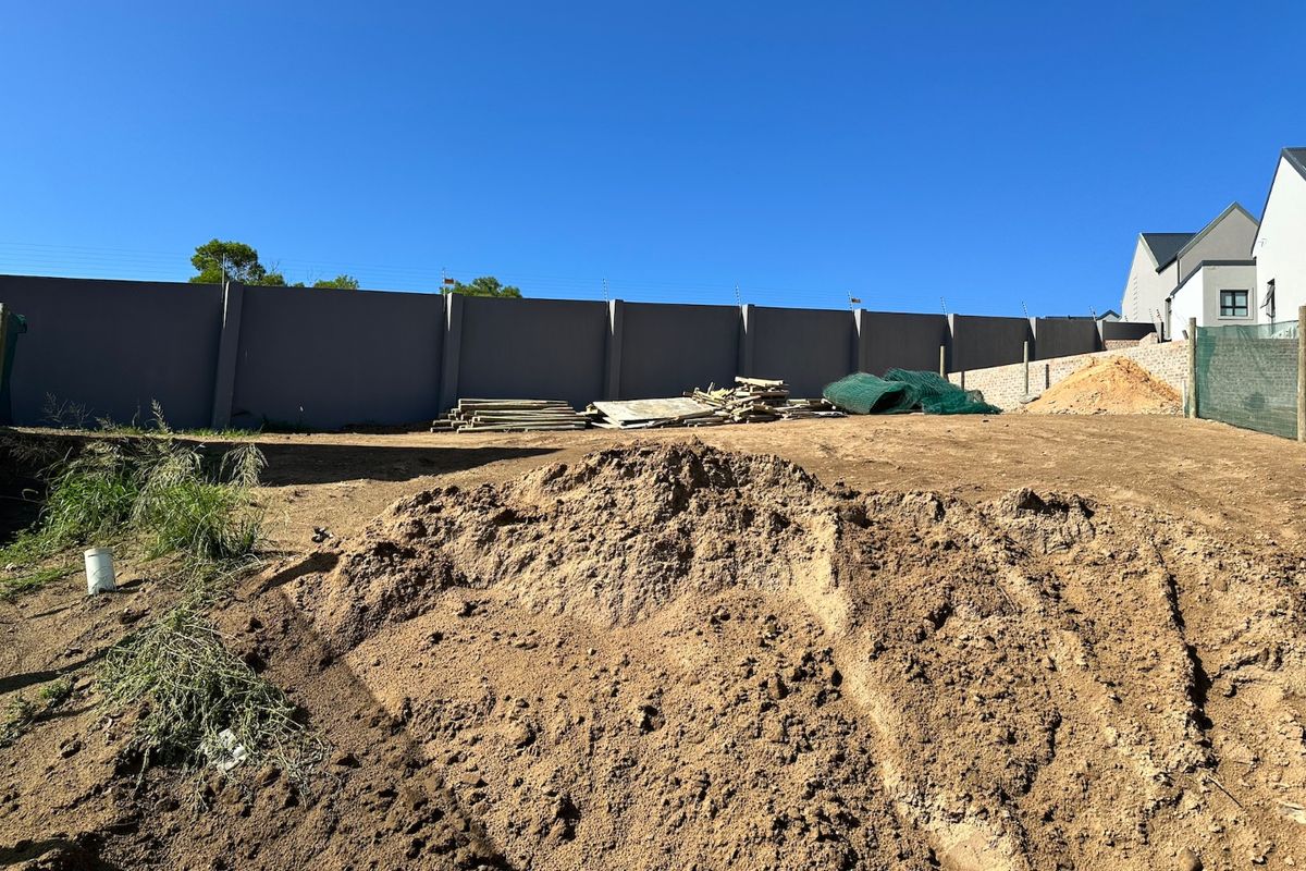 A vacant residential plot featuring a perimeter wall with electric fencing, currently undergoing site preparation with exposed soil and uneven ground.