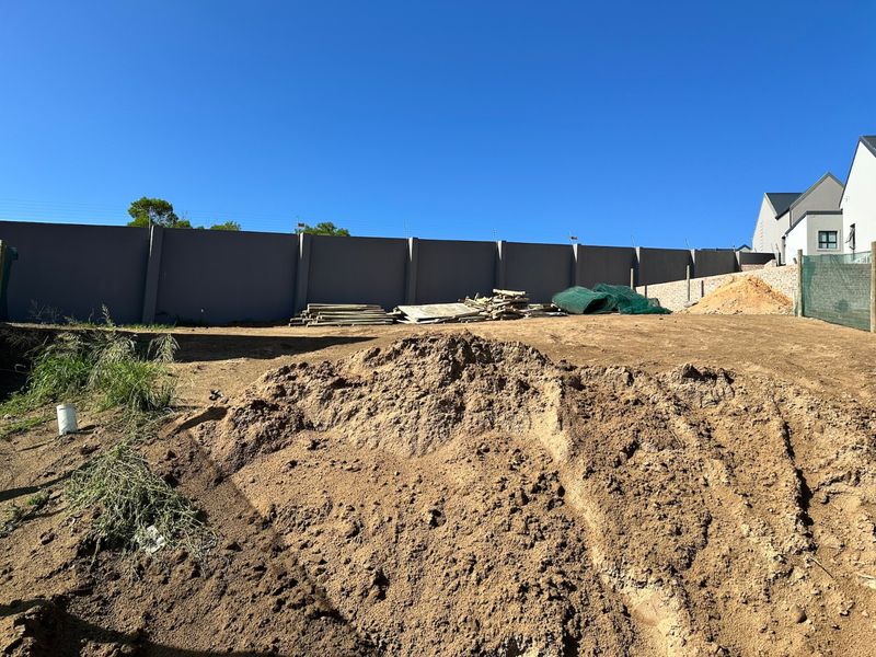 A vacant residential plot featuring a perimeter wall with electric fencing, currently undergoing site preparation with exposed soil and uneven ground.