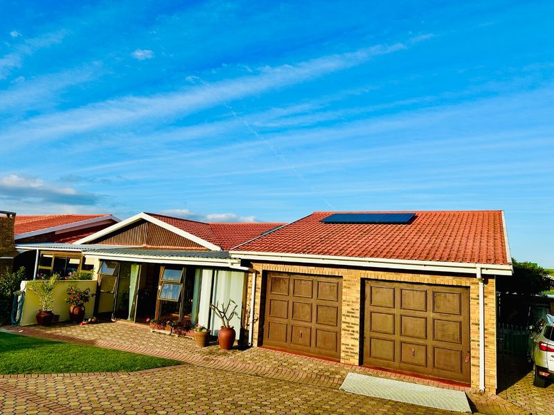 Front view of a townhouse featuring a double garage, tiled roof with solar panels, and a paved driveway.