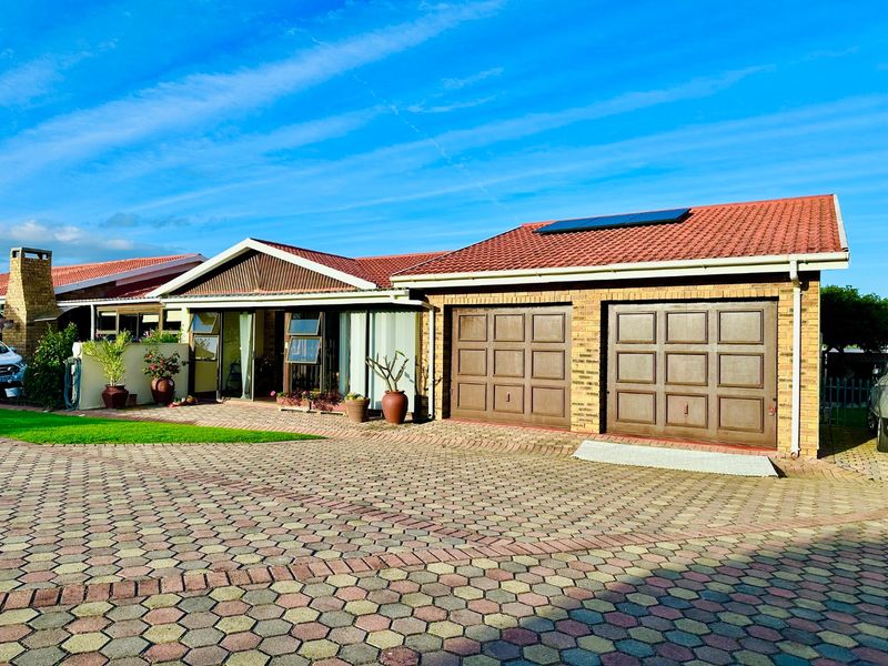 Front view of a townhouse featuring a double garage, paved driveway, and a well-maintained brick facade with a tiled roof and solar panels.