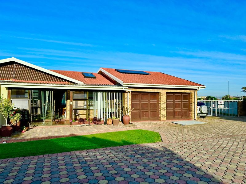 Front view of a townhouse featuring a double garage, paved driveway, solar panels, and a tiled roof with a small garden area.