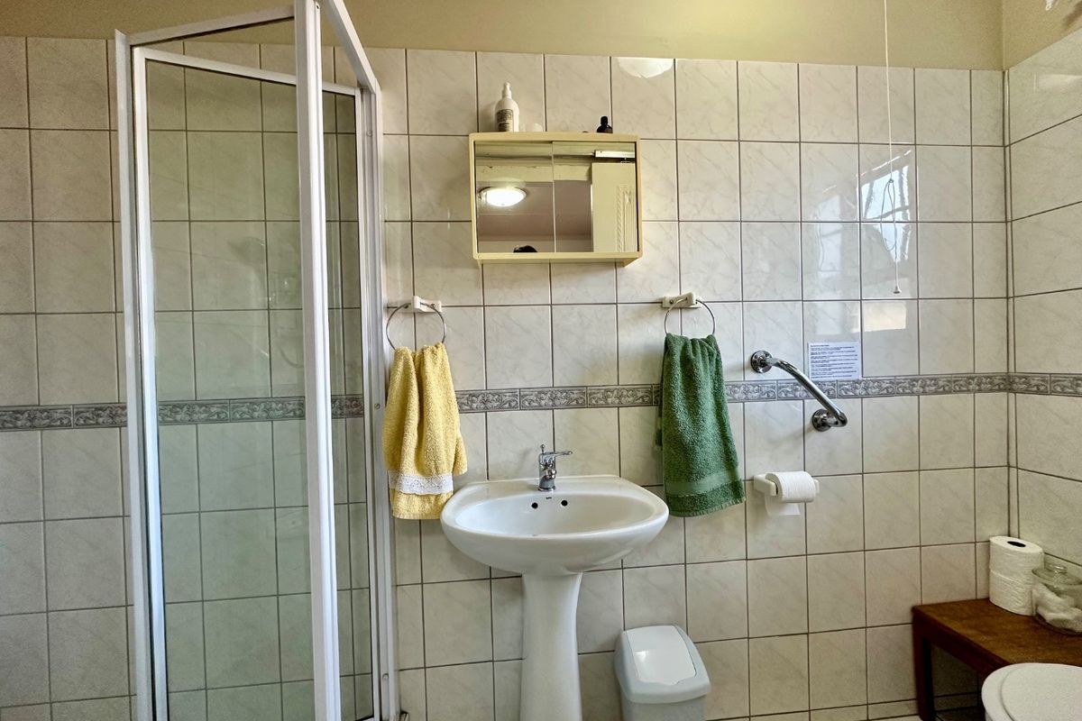 A functional bathroom featuring a pedestal basin, shower enclosure, and wall-mounted medicine cabinet with neutral ceramic wall tiling.