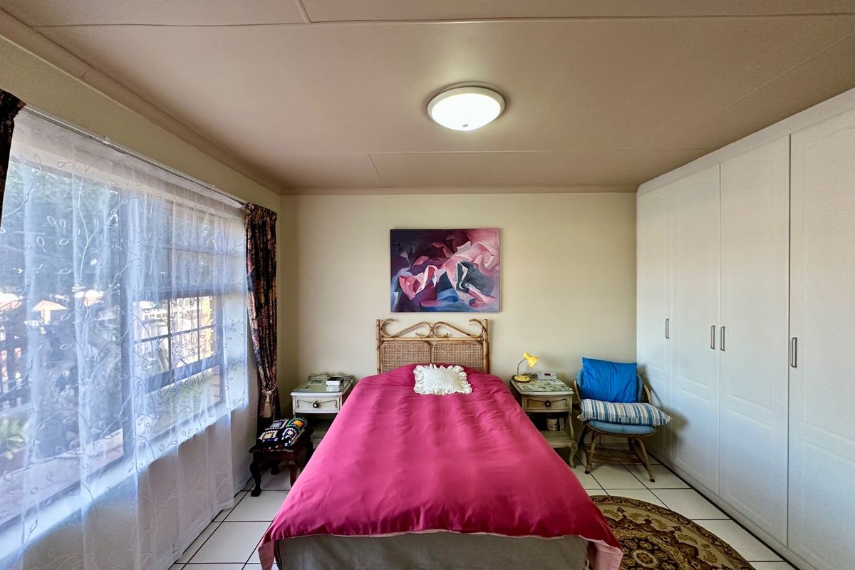 A well-lit bedroom featuring built-in cupboards, tiled flooring, and a large window allowing for natural light.