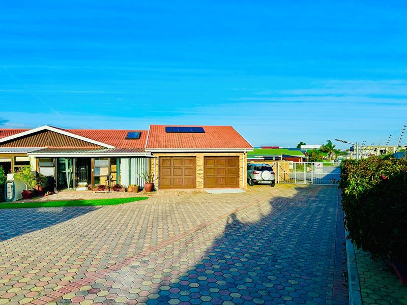 Front view of a townhouse featuring a double garage, paved driveway, and solar panels installed on the tiled roof.