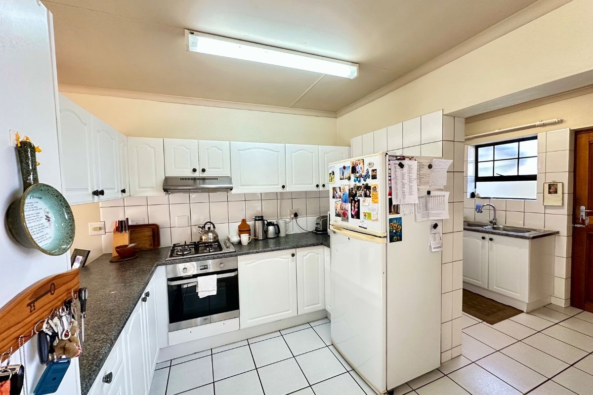 A functional kitchen featuring white cabinetry, gas hob, built-in oven, tiled splashbacks, and an adjoining scullery area with a double sink.