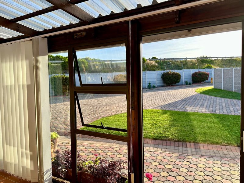 A covered patio area featuring a timber pergola structure with a translucent roof, overlooking a paved driveway and garden area.