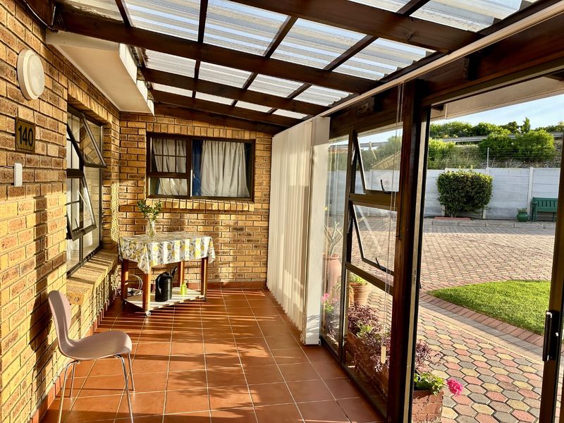 A covered patio area featuring brick walls, tiled flooring, and a timber pergola roof, providing a sheltered outdoor space with views of the paved driveway.