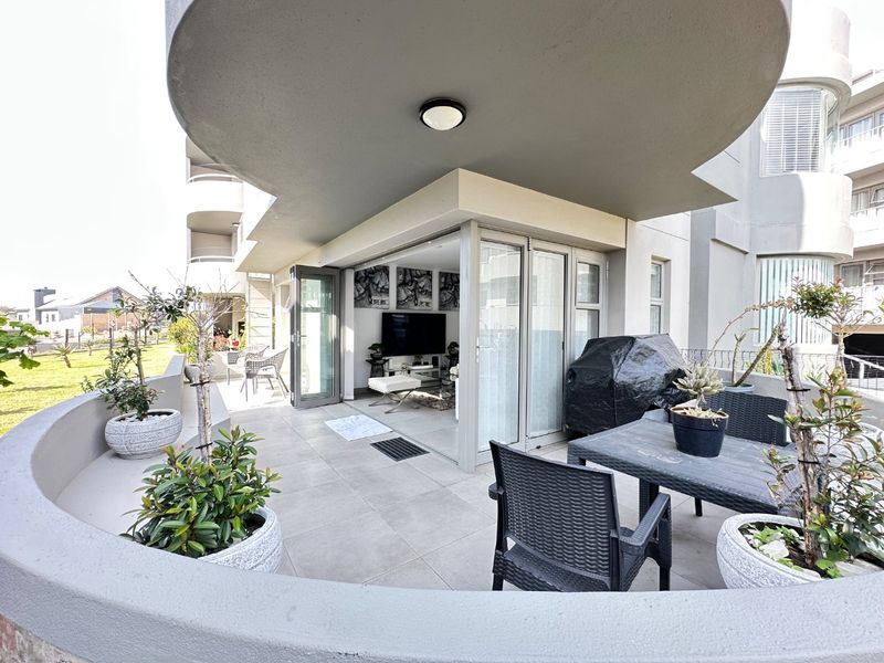 A spacious covered balcony featuring tiled flooring, a curved concrete balustrade, and large sliding glass doors providing seamless access to the interior living area.