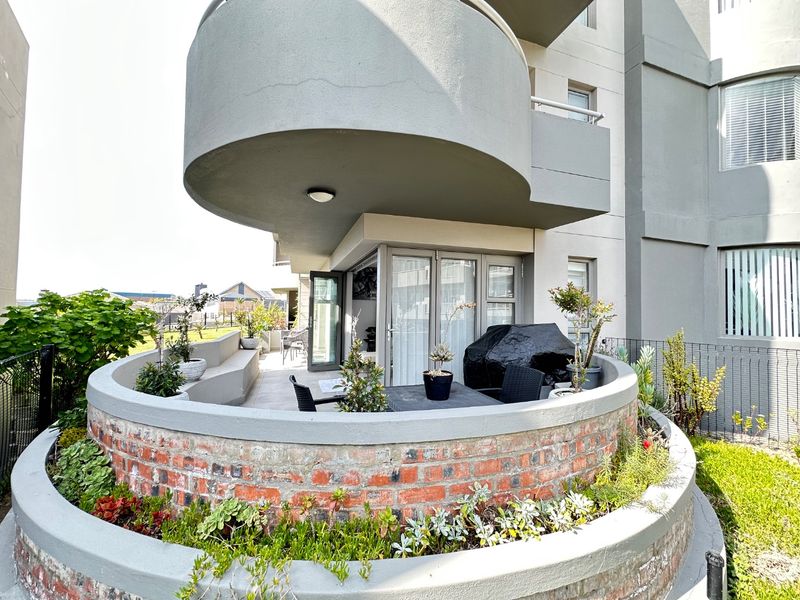 A spacious ground-floor patio featuring a unique curved brick planter, concrete finishes, and direct access to the interior through glass doors.