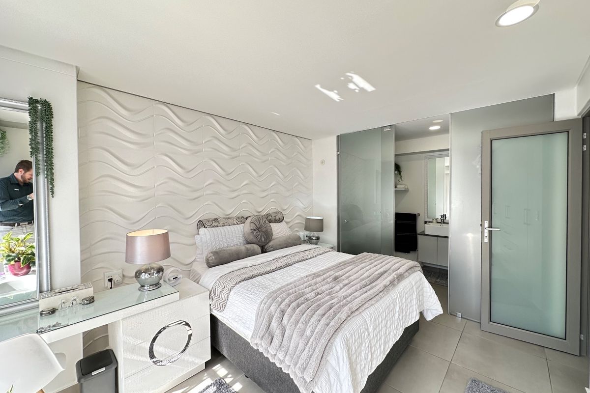 Modern bedroom featuring a textured feature wall, tiled flooring, recessed lighting, and integrated frosted glass doors leading to an en-suite bathroom.