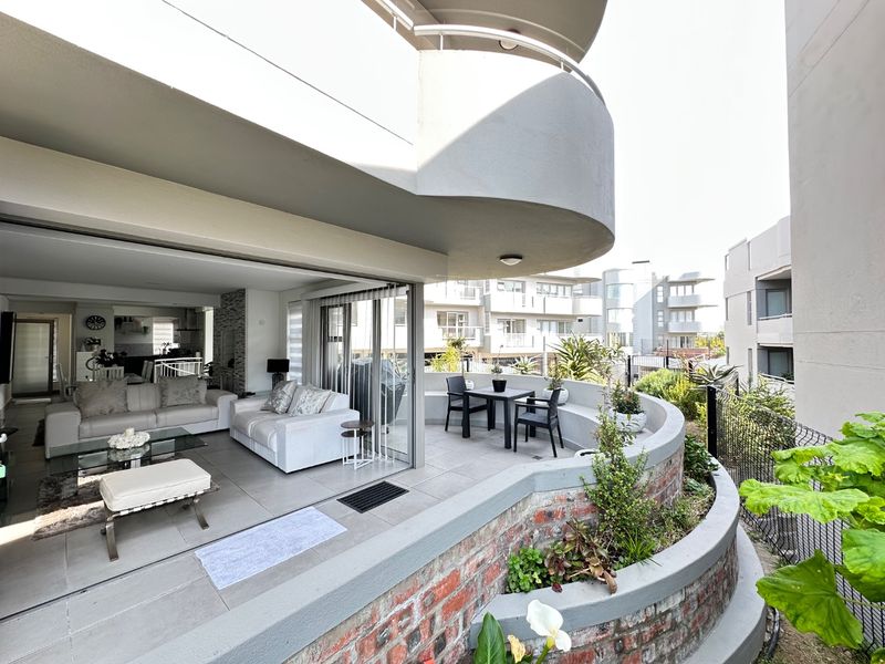 Spacious open-plan living area seamlessly flowing onto a curved balcony with built-in planter boxes and modern tiled finishes.
