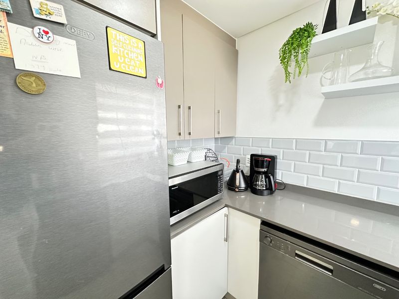 A modern kitchen featuring sleek cabinetry, subway tile backsplash, stone countertops, and integrated appliances including a dishwasher and microwave.