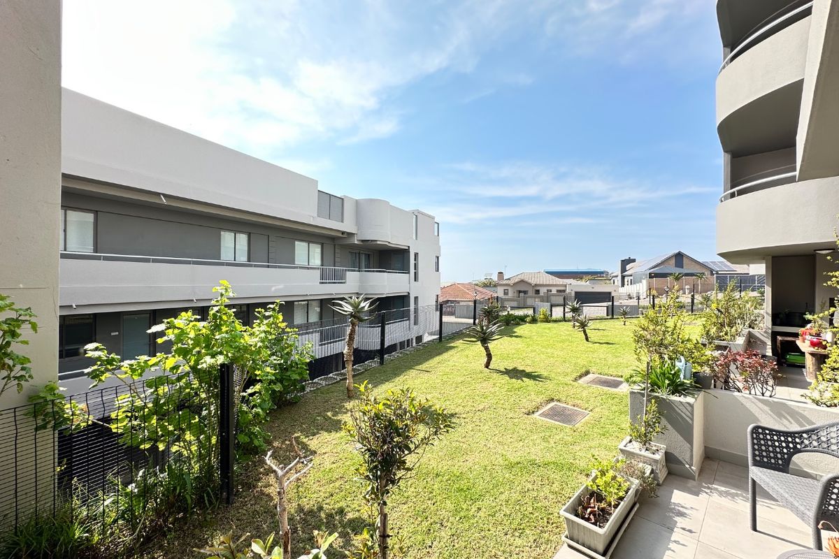 A well-maintained rear garden area featuring a lawn, perimeter fencing, and a tiled balcony overlooking the communal outdoor space.