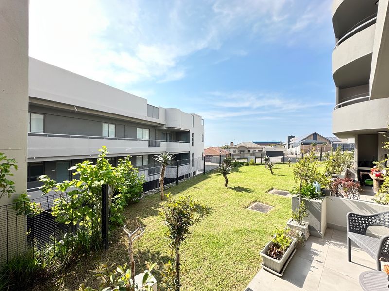 A well-maintained rear garden area featuring a lawn, perimeter fencing, and a tiled balcony overlooking the communal outdoor space.