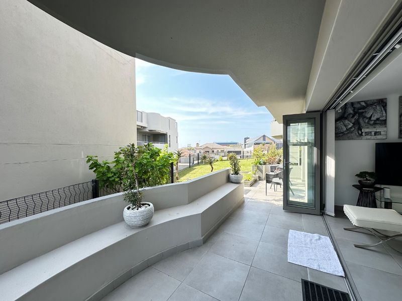 A spacious covered balcony featuring tiled flooring, a built-in concrete bench, and folding glass doors that provide seamless access to the living area.