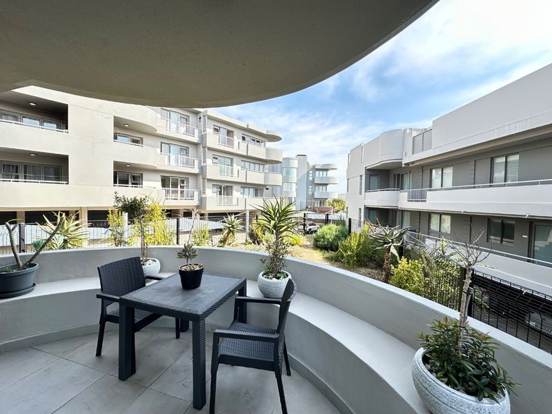 A spacious balcony featuring tiled flooring, a built-in concrete bench, and views over the apartment complex grounds.