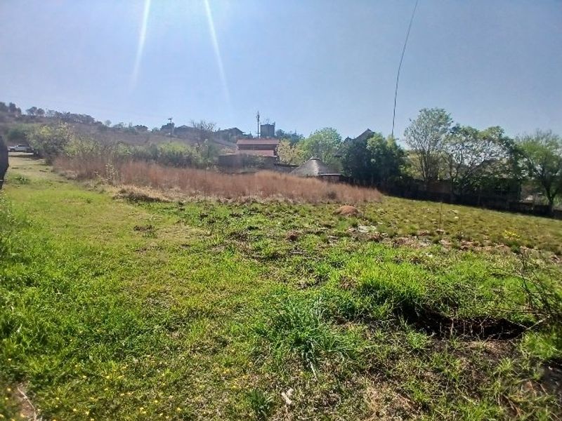 A view of a vacant residential plot featuring natural grassland and a gentle slope, suitable for future development.