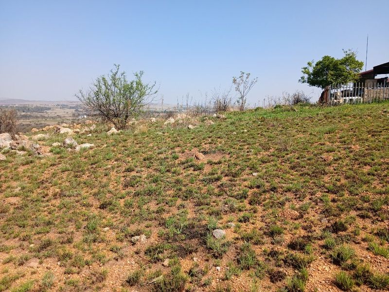 A view of the sloped, undeveloped residential land featuring natural vegetation and rocky terrain under a clear sky.