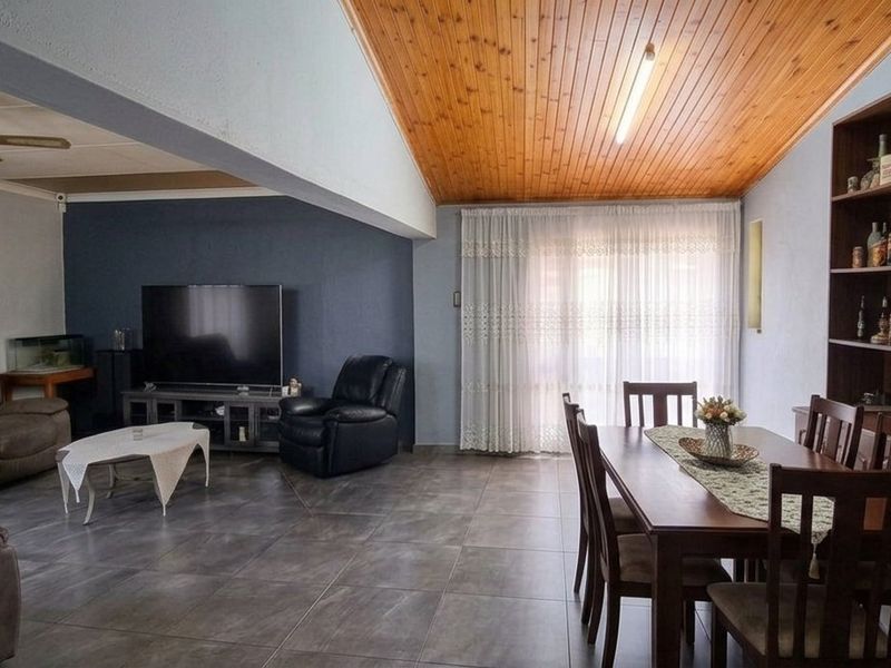 Spacious open-plan living and dining area featuring a vaulted timber-clad ceiling, large format floor tiles, and a built-in display shelving unit.