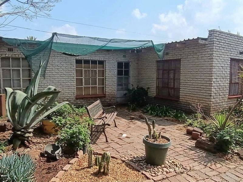 Rear exterior view of a brick house featuring a paved courtyard area, steel-framed windows, and a shade cloth canopy.