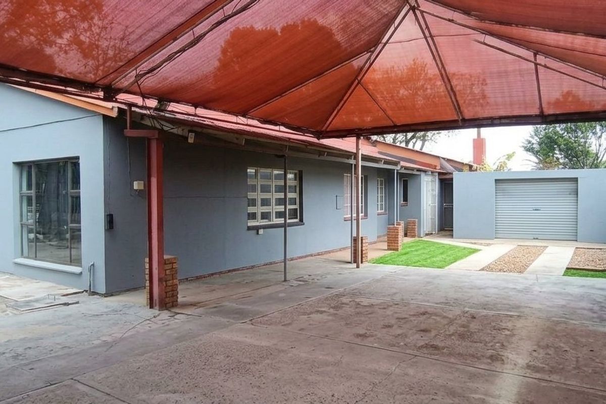 Rear exterior view featuring a large shade cloth canopy, concrete driveway, and a single garage with a brick boundary wall.