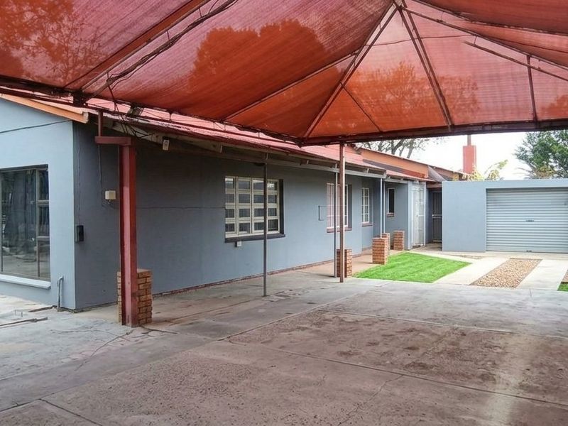 Rear exterior view featuring a large shade cloth canopy, concrete driveway, and a single garage with a brick boundary wall.