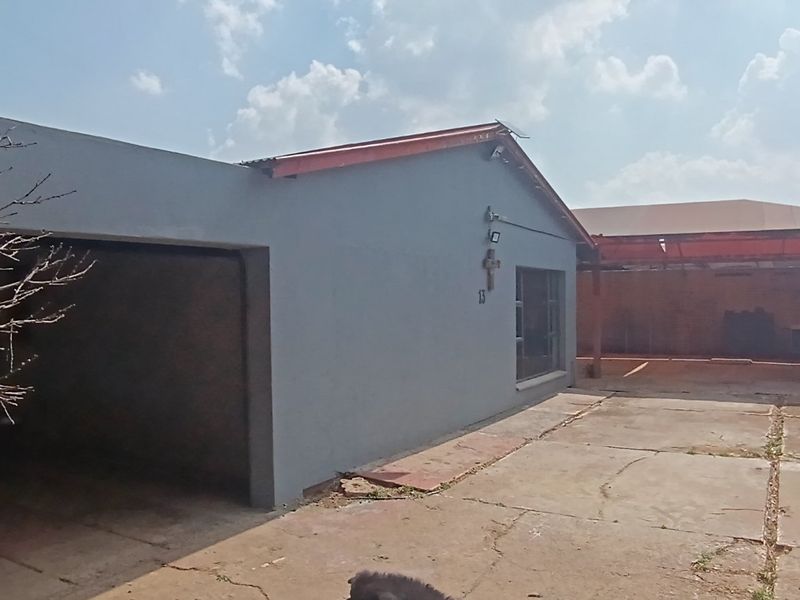 Front exterior view of the property featuring a garage, concrete driveway, and metal roofing, showing signs of wear and weathering.