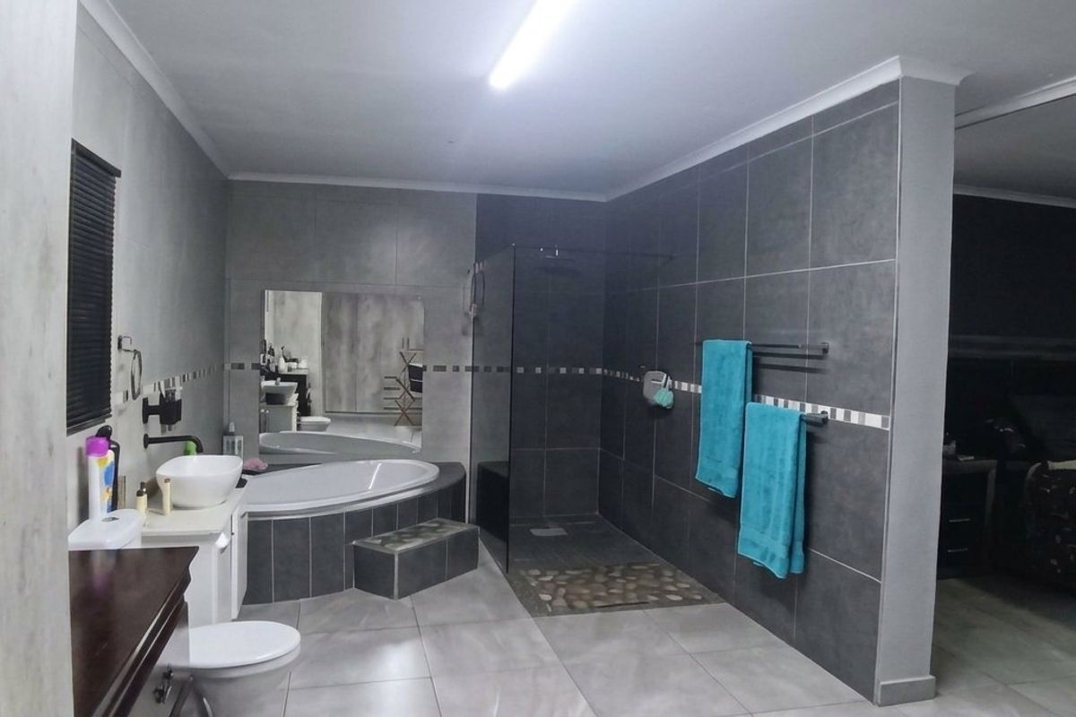 Modern open-plan bathroom featuring a walk-in shower, built-in bathtub, and contemporary grey tiling, seamlessly integrated with the adjacent bedroom area.